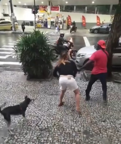 A agressora pega a guia da coleira do cachorro e dá uma espécie de chicotada nas costas de um dos entregadores/Reprodução